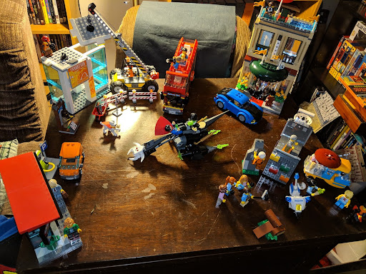 Blurry image with legos on a table and chairs and bookshelf in background.