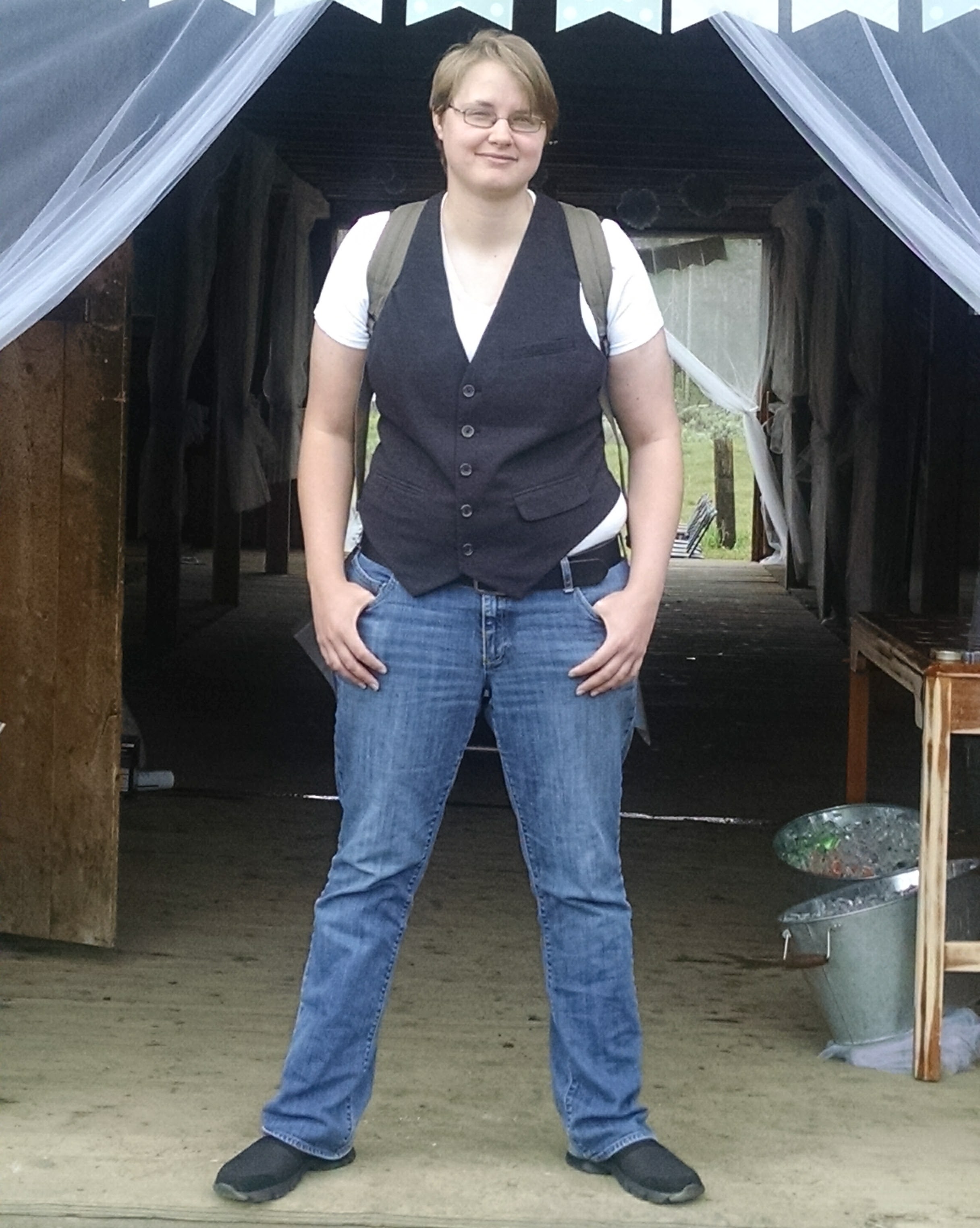 Word Alchemy LLC contributor, The Awkward Ace, is standing in the doorway of a barn and is smiling at the camera in a full-body photo.